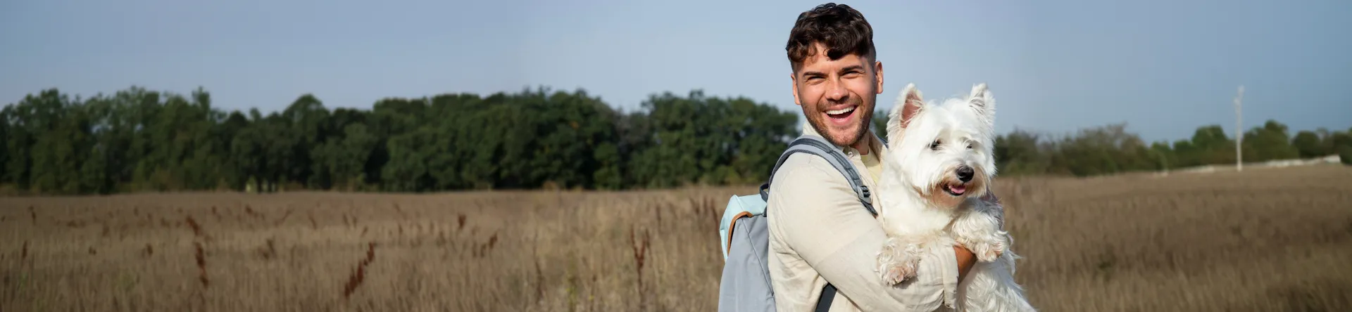 Man smiling with a white dog in a field